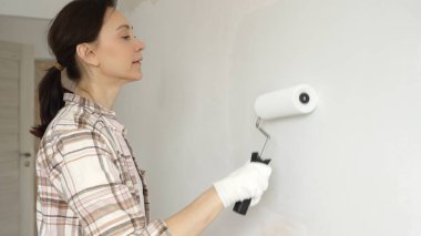 Profesyonel bir ressam koruyucu eldivenler giyerek duvarda pürüzsüz bir şekilde beyaz boya sürüyor, evin içini kusursuz bir fırça ve titiz bir boya tekniğiyle yeniliyor.