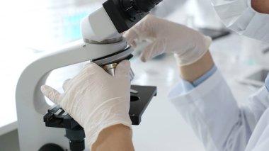 Bilim adamının beyaz eldivenli elleri parlak bir laboratuvarda mikroskobu ayarlıyor, kesinliği vurguluyor ve bilimsel araştırmalara odaklanıyor. Tıp, sağlık ve bilim konsepti.