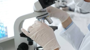Bilim adamının beyaz eldivenli elleri parlak bir laboratuvarda mikroskobu ayarlıyor, kesinliği vurguluyor ve bilimsel araştırmalara odaklanıyor. Tıp, sağlık ve bilim konsepti.