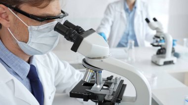 Tıbbi araştırmacı numuneyi mikroskop altında analiz ediyor steril laboratuvar ortamında koruyucu giysiler giyiyor ve bilimsel araştırmalar yapıyor. Tıp, sağlık ve bilim konsepti.