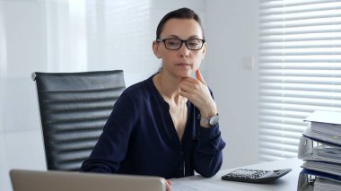 Profesyonel muhasebeci mali tabloları analiz eder, raporları incelerken modern çalışma alanında dizüstü bilgisayar ve evrak işleriyle oturur. İş dünyasında denetim ve vergi teması