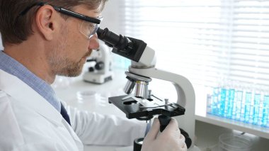 Korumalı giysiler giyerken bilimsel örnekleri analiz eden profesyonel bir araştırmacı, cam ekipmanlarla steril laboratuvar ortamında dikkatlice çalışıyor. Tıp, sağlık ve bilim konsepti