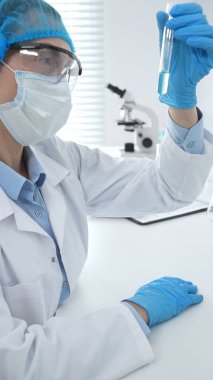 Mavi kapaklı, eldivenli ve Google 'lı tıp bilimi araştırmacısı laboratuvar çalışma alanında test tüpündeki sıvıyı inceliyor. İlaç ve sağlık hizmetleri kavramı.