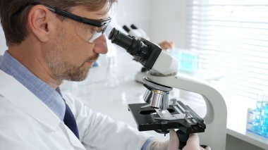 Korumalı giysiler giyerken bilimsel örnekleri analiz eden profesyonel bir araştırmacı, cam ekipmanlarla steril laboratuvar ortamında dikkatlice çalışıyor. Tıp, sağlık ve bilim konsepti