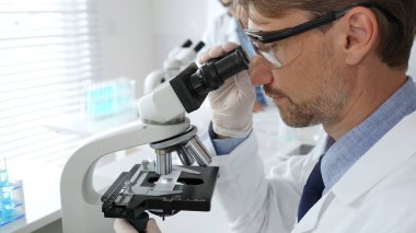 Korumalı giysiler giyerken bilimsel örnekleri analiz eden profesyonel bir araştırmacı, cam ekipmanlarla steril laboratuvar ortamında dikkatlice çalışıyor. Tıp, sağlık ve bilim konsepti