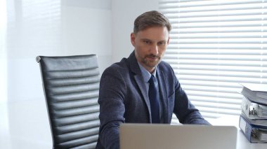 Profesyonel iş adamı dizüstü bilgisayarla uğraşırken yakın çevresindeki organize klasörlerle şık çalışma sahalarında konumlanıyor ve kurumsal ithafı vurguluyor. İş dünyasında denetim ve vergi teması