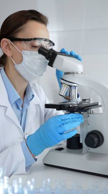 Maske takan kadın bilim adamı ve mavi eldivenli mikroskop kullanarak modern laboratuvarda bilimsel araştırmalar yapıyor. Tıp, sağlık ve bilim konsepti.