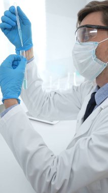 Koruyucu giysi giyen bilim araştırmacısı modern laboratuvar çalışma alanında mavi sıvı numunesini test tüpünden inceliyor. Tıp, sağlık ve bilim konsepti