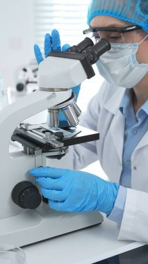 Kadın bilim adamı mikroskop ile numune analiz ediyor, tıbbi araştırma sırasında koruyucu laboratuvar giysileri giyiyor. Tıp, laboratuvar ve bilim konsepti.