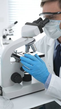 Koruyucu Google ve mavi eldiven giyen bilim adamı mikroskop kullanarak modern laboratuvarda bilimsel araştırmalar yapıyor. Tıp ve bilim konsepti.