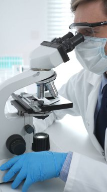 Koruyucu Google ve mavi eldiven giyen bilim adamı mikroskop kullanarak modern laboratuvarda bilimsel araştırmalar yapıyor. Tıp ve bilim konsepti.