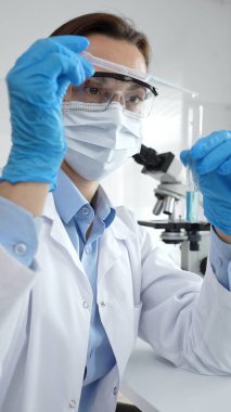 Bilimadamları laboratuvar tıbbi araştırma çalışmaları sırasında koruyucu giysi giyip tüpü hassas pipetle test etmek için kimyasal sıvı eklediler. Tıp, sağlık ve bilim konsepti