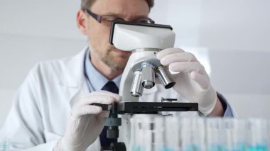 Beyaz koruyucu eldivenler giyen insan bilim araştırmacısı laboratuvar mikroskobunu dikkatlice kalibre ederek hassas tıbbi araştırmalar yapıyor. Tıp, sağlık ve bilim konsepti.