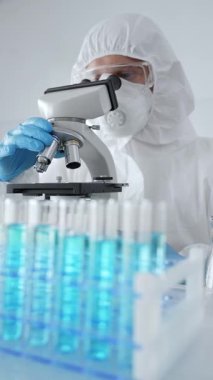 Koruyucu ekipman takan bilim araştırmacısı mikroskobu ayarlıyor, laboratuvar örneklerini steril araştırma ortamında hassasiyetle analiz ediyor. Tıp, sağlık ve bilim konsepti.