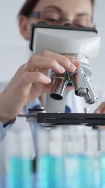 Kadın laboratuar bilimcisi mikroskop kayışını dikkatlice yerleştiriyor. Laboratuvarda araştırma hassasiyetini gösteriyor. Tıp, sağlık ve bilim konsepti.