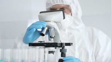 Koruyucu ekipman takan bilim araştırmacısı mikroskobu ayarlıyor, laboratuvar örneklerini steril araştırma ortamında hassasiyetle analiz ediyor. Tıp, sağlık ve bilim konsepti.