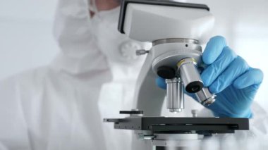 Laboratuvar araştırması sırasında mavi koruyucu eldiven takan bilim araştırmacısı ince ayar mikroskobu lensleri takıyor. Tıp, sağlık ve bilim konsepti.