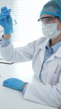 Mavi kapaklı, eldivenli ve Google 'lı tıp bilimi araştırmacısı laboratuvar çalışma alanında test tüpündeki sıvıyı inceliyor. İlaç ve sağlık hizmetleri kavramı.