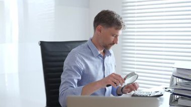 Muhasebeci, mali belgeleri büyüteçle dikkatlice inceleyerek ofisinin çalışma alanındaki detaylara hassasiyet ve dikkat sağlamış. İş dünyasında denetim ve vergi teması