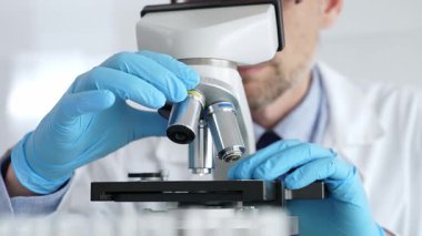 Beyaz önlüklü ve mavi eldivenli, mikroskop ayarlayan, modern laboratuarda ilaç araştırması yapan erkek bilim adamlarına yaklaş. Tıp ve bilim konsepti.