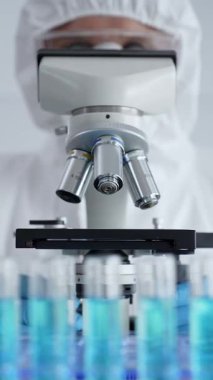 Koruyucu ekipman takan bilim araştırmacısı mikroskobu ayarlıyor, laboratuvar örneklerini steril araştırma ortamında hassasiyetle analiz ediyor. Tıp, sağlık ve bilim konsepti.
