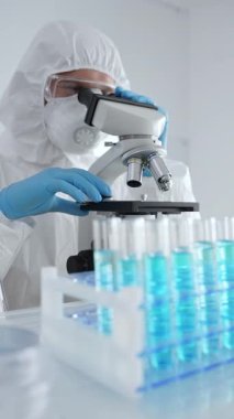 Koruyucu ekipman takan bilim araştırmacısı mikroskobu ayarlıyor, laboratuvar örneklerini steril araştırma ortamında hassasiyetle analiz ediyor. Tıp, sağlık ve bilim konsepti.