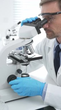 Mavi eldiven giyen tıp bilimcisi mikroskop kullanarak modern laboratuvarda bilimsel araştırma yapıyor. Tıp, sağlık ve bilim konsepti.