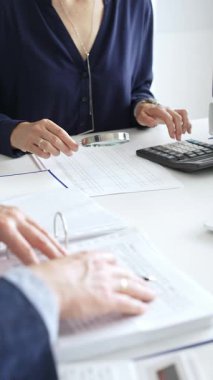 İş yerindeki kurumsal verileri incelerken, büyüteç ve hesap makinesi kullanarak, erkek meslektaşlarıyla birlikte belgeleri inceleyen kadın mali analistler. Ticarette denetim ve vergiler.