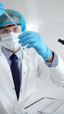 Steril laboratuvar çalışma alanı içindeki pipeti kullanarak turkuaz sıvı örneğini inceleyen koruyucu ekipman giyen bir bilim adamı. Tıp, sağlık ve bilim konsepti