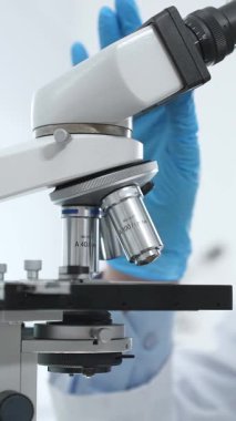 Modern laboratuvar ortamında mikroskobu ayarlayan mavi eldivenli bilim adamlarına yakın çekim. Tıp, bilim ve sağlık hizmetleri kavramı.