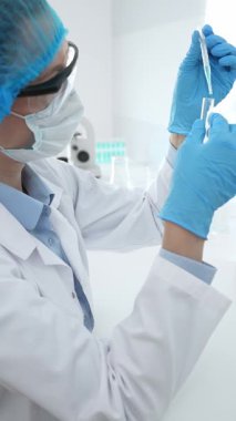 Mavi kapaklı, eldivenli ve Google 'lı tıp bilimi araştırmacısı laboratuvar çalışma alanında test tüpündeki sıvıyı inceliyor. İlaç ve sağlık hizmetleri kavramı.