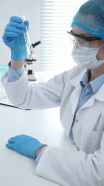 Mavi kapaklı, eldivenli ve Google 'lı tıp bilimi araştırmacısı laboratuvar çalışma alanında test tüpündeki sıvıyı inceliyor. İlaç ve sağlık hizmetleri kavramı.