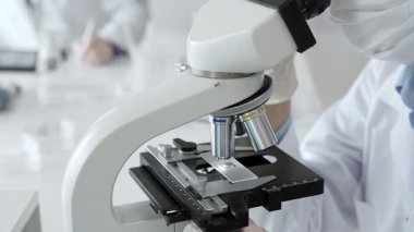 Beyaz koruyucu eldivenler giyen bilim teknisyeni laboratuvar mikroskobunu dikkatlice ayarlıyor ve titiz bir araştırma tekniği sergiliyor. Tıp, sağlık ve bilim konsepti