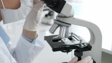 Beyaz koruyucu eldivenler giyen bilim teknisyeni laboratuvar mikroskobunu dikkatlice ayarlıyor ve titiz bir araştırma tekniği sergiliyor. Tıp, sağlık ve bilim konsepti