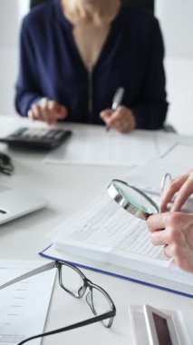 Ofisteki iş yerinde büyüteç ve hesap makinesi kullanarak kadın meslektaşlarıyla birlikte belgeleri inceleyen erkek mali analistleri kapatın. Ticarette denetim ve vergiler.