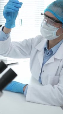 Mavi kapaklı, eldivenli ve Google 'lı tıp bilimi araştırmacısı laboratuvar çalışma alanında test tüpündeki sıvıyı inceliyor. İlaç ve sağlık hizmetleri kavramı.