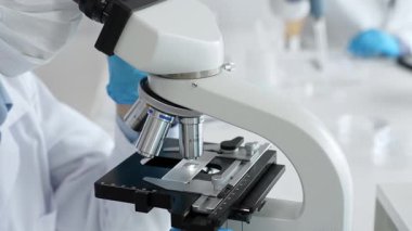 Mikroskop merceklerini inceleyen mavi koruyucu giysiler giyen, detaylı tıbbi laboratuvar araştırmaları yapan bilim adamlarına yaklaş. Tıp, sağlık ve bilim konsepti.