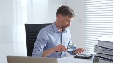 Muhasebeci, mali belgeleri büyüteçle dikkatlice inceleyerek ofisinin çalışma alanındaki detaylara hassasiyet ve dikkat sağlamış. İş dünyasında denetim ve vergi teması