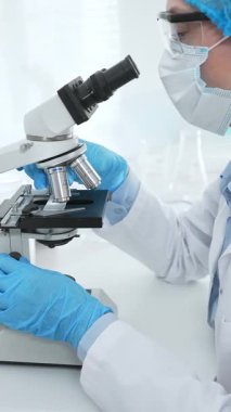 Mavi koruyucu giysili kadın bilim adamı laboratuvar araştırma ortamında test örneklerini mikroskop altında analiz ediyor. Tıp, sağlık ve bilim konsepti.