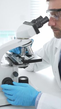 Mavi eldiven giyen tıp bilimcisi mikroskop kullanarak modern laboratuvarda bilimsel araştırma yapıyor. Tıp, sağlık ve bilim konsepti.