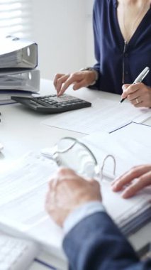 İş yerindeki kurumsal verileri incelerken, büyüteç ve hesap makinesi kullanarak, erkek meslektaşlarıyla birlikte belgeleri inceleyen kadın mali analistler. Ticarette denetim ve vergiler.