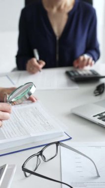 Ofisteki iş yerinde büyüteç ve hesap makinesi kullanarak kadın meslektaşlarıyla birlikte belgeleri inceleyen erkek mali analistleri kapatın. Ticarette denetim ve vergiler.