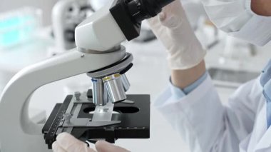 Beyaz koruyucu eldivenler giyen bilim teknisyeni laboratuvar mikroskobunu dikkatlice ayarlıyor ve titiz bir araştırma tekniği sergiliyor. Tıp, sağlık ve bilim konsepti