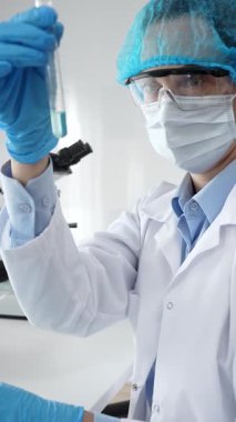 Steril laboratuvar ortamında tıbbi araştırma sırasında mikroskop yakınında mavi sıvı numunesini inceleyen koruyucu ekipman giyen bilim adamları. Tıp, sağlık ve bilim konsepti