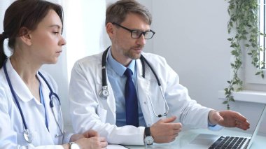 İki doktor bir dizüstü bilgisayarda tıbbi çizelgeleri inceliyor, hastane veya klinik ortamdaki hasta verilerini tartışıyorlar. Tıp ve sağlık hizmetleri kavramı