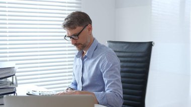 Bir ofis ortamında mali raporları incelerken faturaları hesaplayan ve yöneten profesyonel bir muhasebeci. İş dünyasında denetim ve vergi teması.