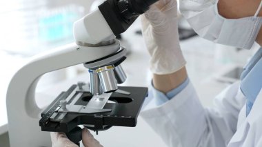 Laboratuar mikroskobunu dikkatlice ayarlayan koruyucu eldivenler giyen bilim teknisyeni titiz bir araştırma tekniği sergiliyor. Tıp, sağlık ve bilim konsepti