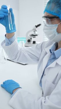Mavi kapaklı, eldivenli ve Google 'lı tıp bilimi araştırmacısı laboratuvar çalışma alanında test tüpündeki sıvıyı inceliyor. İlaç ve sağlık hizmetleri kavramı.
