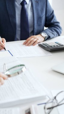 İş adamları mali belgeleri büyüteç ve hesap makinesiyle inceliyor, verileri analiz ediyor ve ofiste raporlar hazırlıyorlar. İş dünyasında denetim ve vergi teması