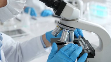 Mikroskop merceklerini inceleyen, detaylı tıbbi laboratuvar araştırmaları yapan mavi eldivenli eldiveni kapatın. Tıp, sağlık ve bilim konsepti.